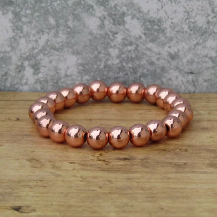 Roségold hematit ásvány karkötő fényes rézszínű gyöngyökkel fa felületen